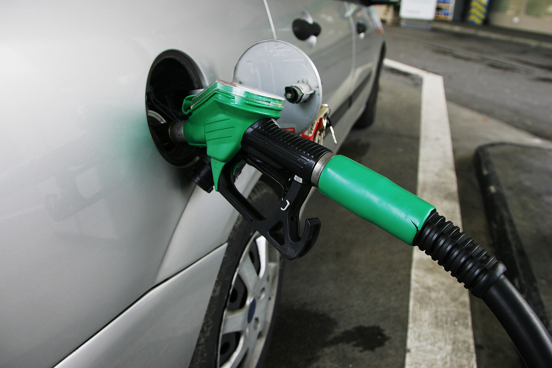 Green fuel nozzle inserted into a silver vehicle at a filling station