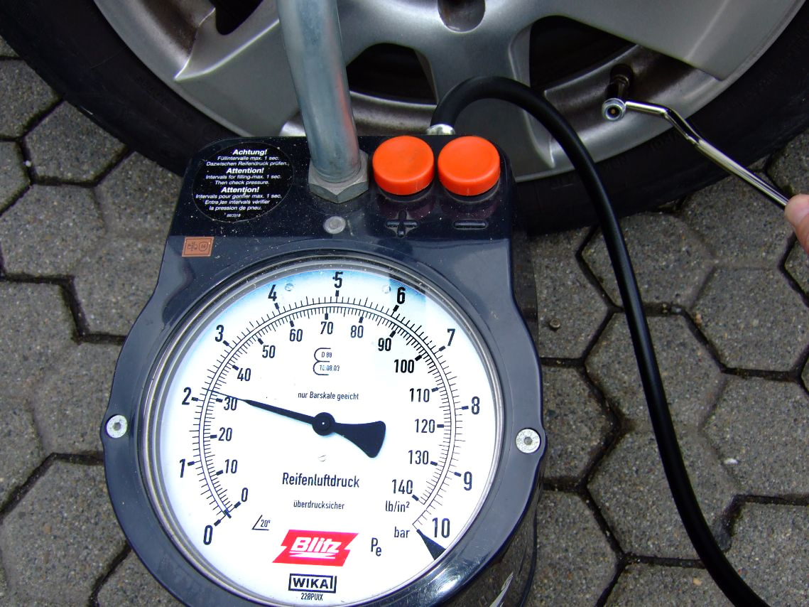 A pressure gauge and hose at a car wheel during a tyre-pressure check